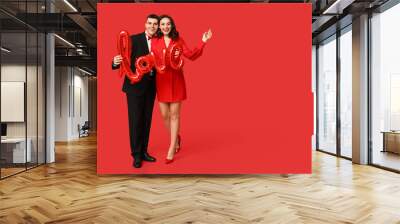 Loving young couple with balloon in shape of word LOVE on red background. Celebration of Saint Valentine's Day Wall mural