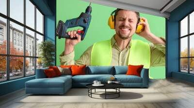 Male builder in hearing protectors with drill on green background Wall mural