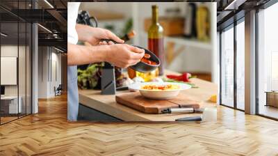 Male chef adding tasty sauce into plate with pasta in kitchen, closeup Wall mural