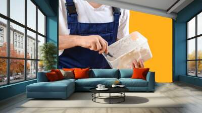 Male decorator with putty knife and plaster on yellow background, closeup Wall mural