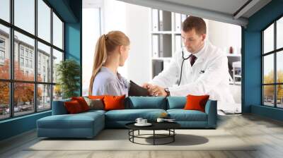 Male doctor measuring blood pressure of female patient in hospital Wall mural