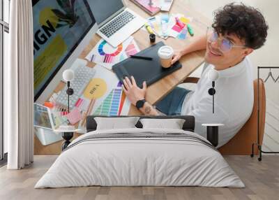 Male graphic designer with cup of coffee working at table in office Wall mural