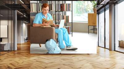 Male medical student studying with laptop in library Wall mural