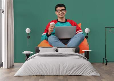 Male programmer with cup of coffee and laptop sitting on green background Wall mural