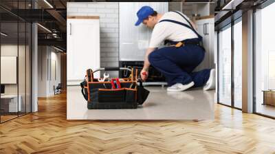 Male worker with tools repairing refrigerator in kitchen Wall mural