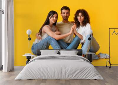 Man and two beautiful women on color background. Polyamory concept Wall mural