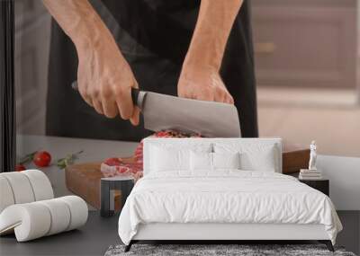 Man cutting fresh raw meat on wooden board in kitchen Wall mural