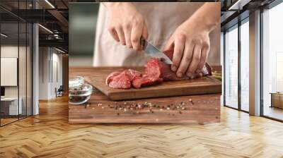 Man cutting raw meat on wooden board in kitchen Wall mural