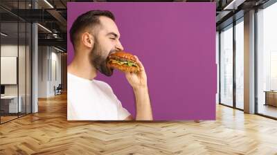 Man eating tasty burger on color background Wall mural