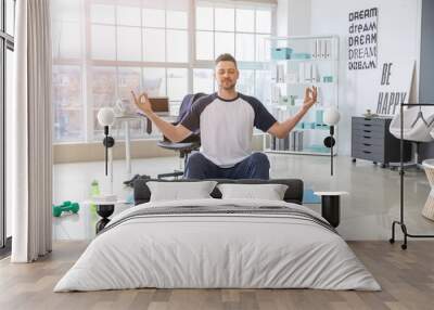 Man meditating on fitness ball in office Wall mural