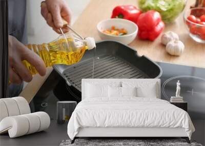 Man pouring sunflower oil on frying pan in kitchen Wall mural