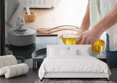 Man pouring sunflower oil on frying pan in kitchen Wall mural