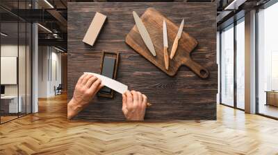 Man sharpening knife on wooden background Wall mural