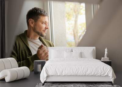 Man with cup of tea relaxing near window at home Wall mural