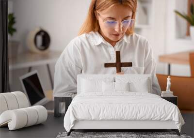 Mature businesswoman with cross praying in office Wall mural