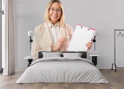 Mature female math teacher with clipboard and pen on grey background Wall mural