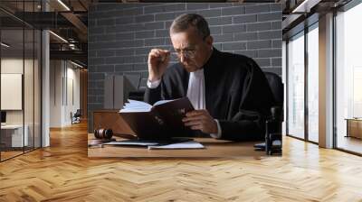 Mature judge reading law book at table in office Wall mural