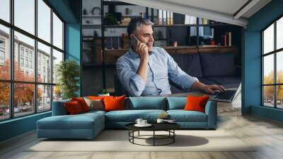 Mature man talking by phone while working on laptop in office Wall mural