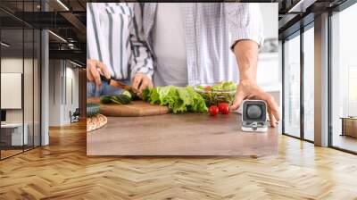 Mature man with hearing aid and his wife cooking in kitchen Wall mural