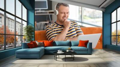 Mature man with laptop and headphones sitting on sofa at home Wall mural