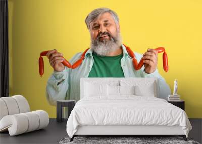 Mature man with tasty sausages on yellow background Wall mural