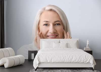 Mature woman giving herself face massage on light background Wall mural