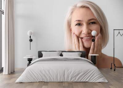 Mature woman giving herself face massage on light background Wall mural