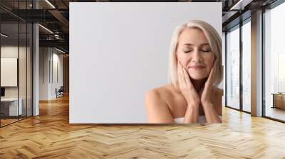 mature woman giving herself face massage on light background Wall mural