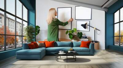 Mature woman hanging blank frame on light wall at home Wall mural