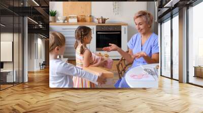 Mature woman receiving gifts from her little grandchildren in kitchen. International Women's Day Wall mural