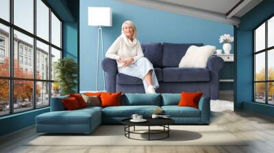 Mature woman sitting on blue sofa at home Wall mural