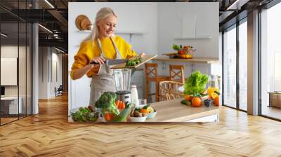 Mature woman with cut avocado making healthy smoothie in kitchen Wall mural