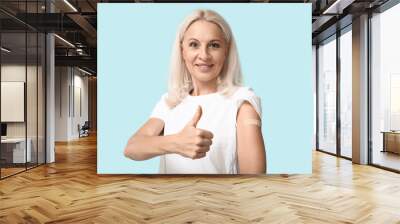 Mature woman with medical patch on arm showing thumb-up against blue background. Vaccination concept Wall mural