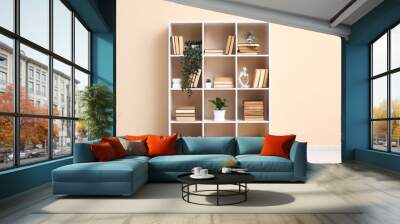 Modern shelving unit with books and home decor near beige wall Wall mural