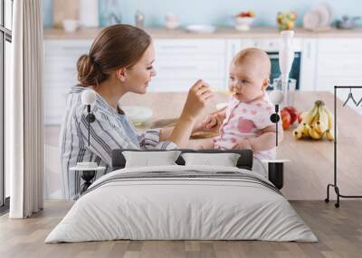 Mother feeding her little baby in kitchen at home Wall mural