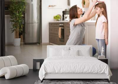 Mother measuring height of little girl near wall Wall mural