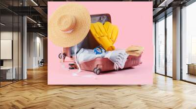 Open suitcase with beach accessories on pink background Wall mural