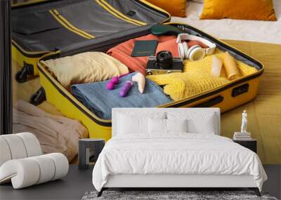 Open suitcase with clothes, sex toys, cosmetics and photo camera on bed Wall mural