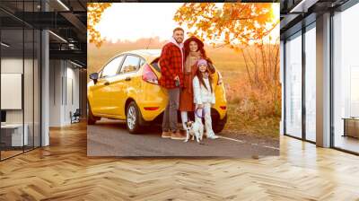 Parents with little daughter and cute dog near yellow car on autumn day Wall mural