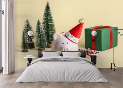 Piggy bank in festive party hat with Christmas trees, gift box and candy canes on beige background Wall mural