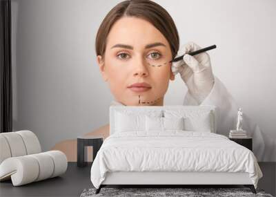 Plastic surgeon applying marking on female face against light background Wall mural