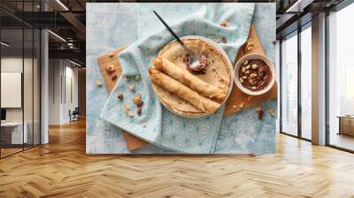 Plate of tasty thin pancakes with chocolate paste and nuts on blue background Wall mural