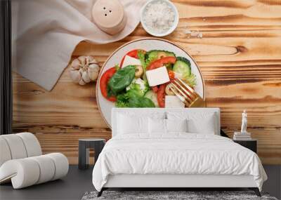 Plate with healthy vegetable salad, napkin, fork and garlic on wooden background Wall mural