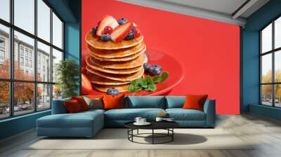 Plate with tasty pancakes, strawberry and blueberries on red background Wall mural