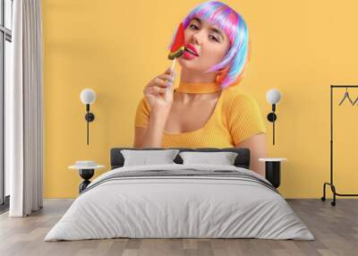 Portrait of beautiful young woman in colorful wig with watermelon candy on orange background Wall mural