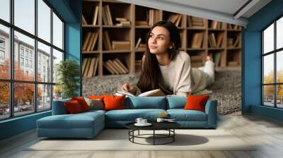 Portrait of beautiful young woman with book in library Wall mural