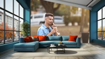 Portrait of handsome businessman with cup of coffee talking by phone outdoors Wall mural