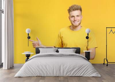 Portrait of handsome young man pointing at something on color background Wall mural