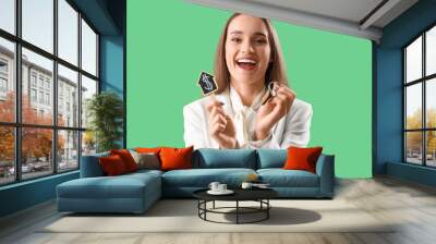 Portrait of happy female real estate agent holding house figure with dollar sign and keys on green background Wall mural