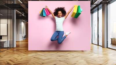 Portrait of jumping African-American woman with shopping bags on color background Wall mural